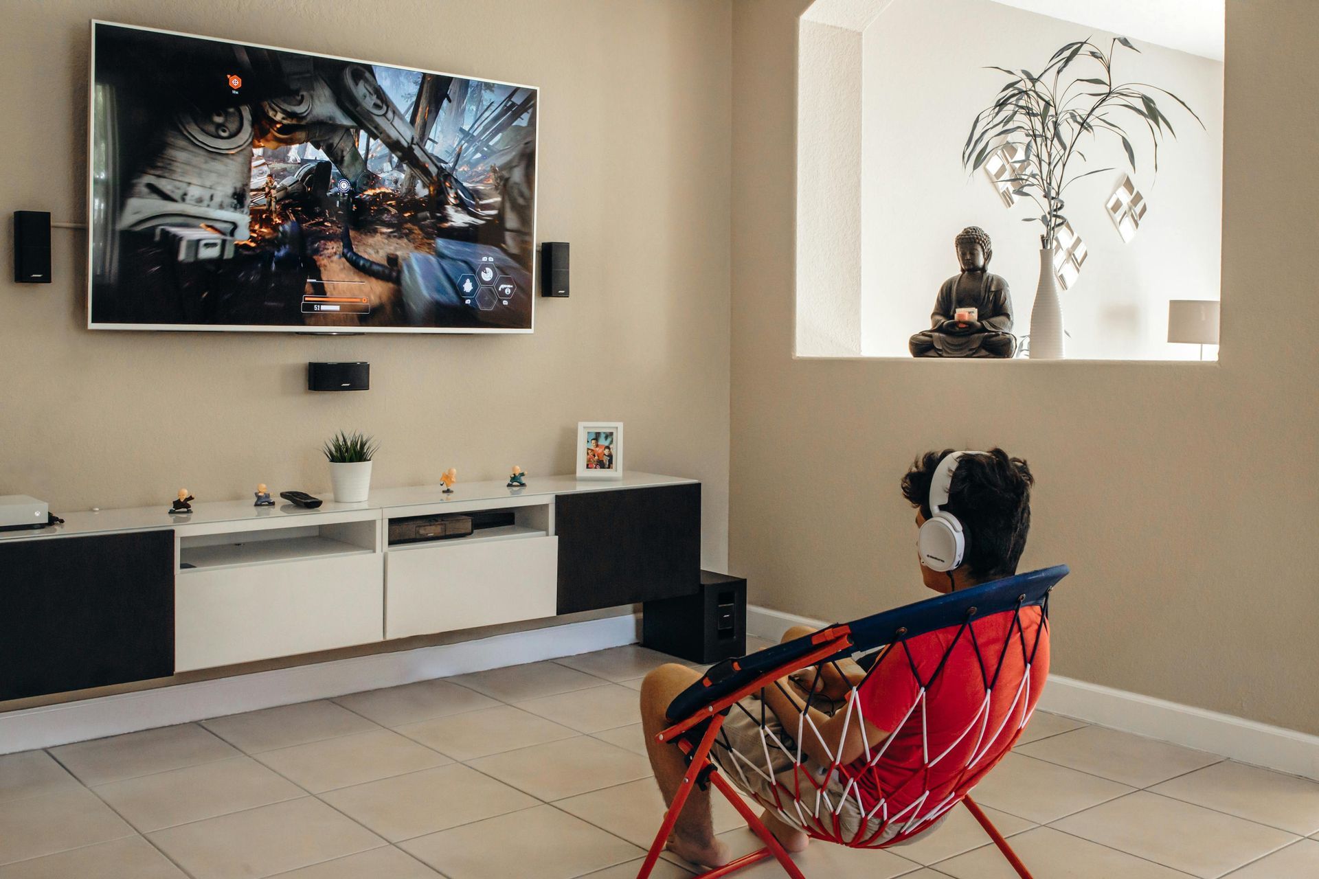 A person sitting in a colorful folding chair wearing headphones while playing a video game on a large wall-mounted TV.