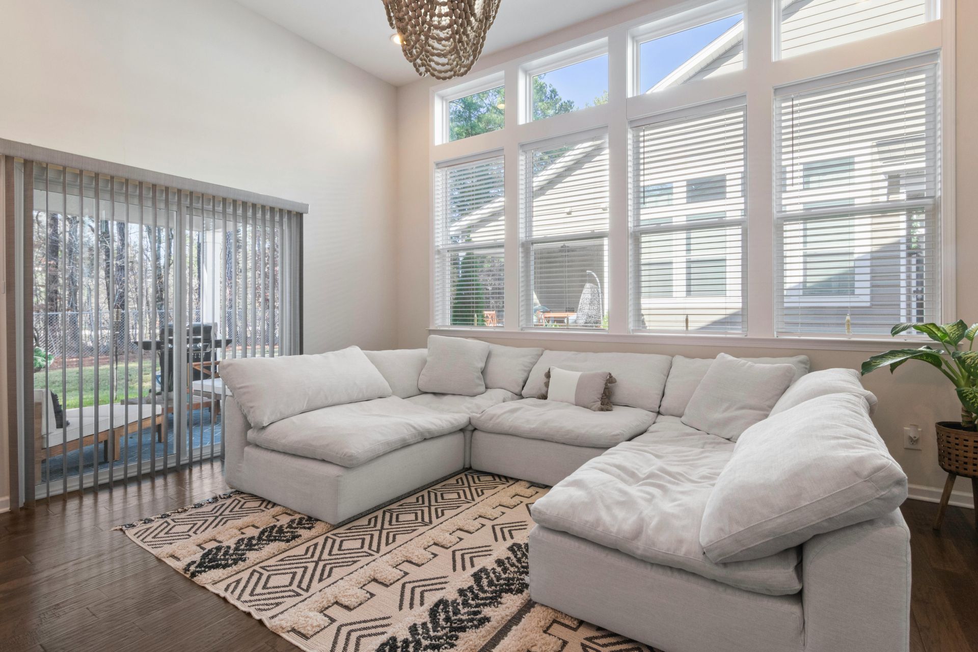 Bright living room with a white sectional sofa, patterned rug, and large windows with blinds.