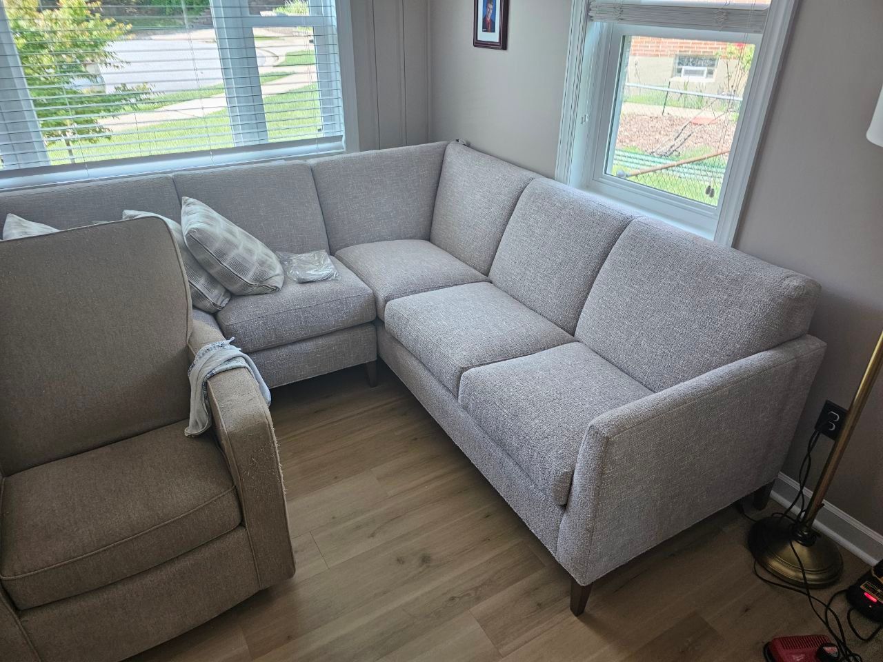 Beige sectional sofa in a room with a recliner and windows.