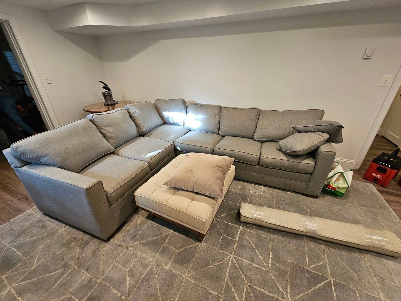 Gray sectional sofa and ottoman on a patterned rug in a room.