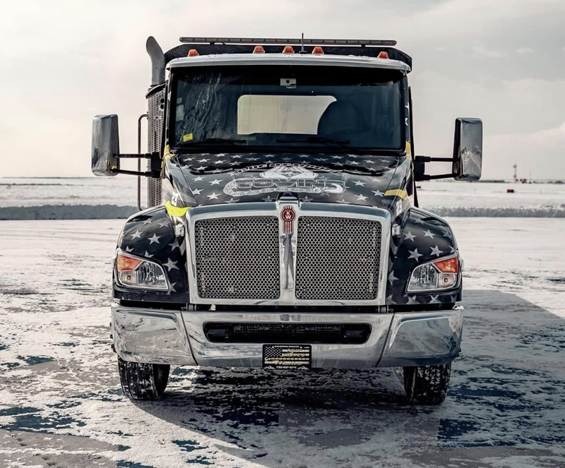 Front view of a black semi-truck with American flag design on snow.