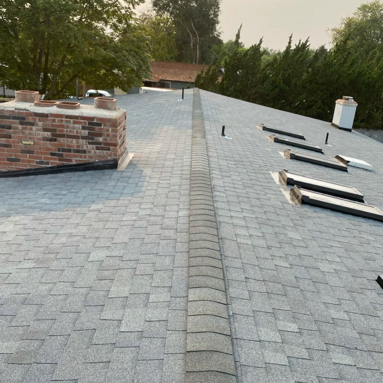 Gray shingled roof with a brick chimney and vent pipes.