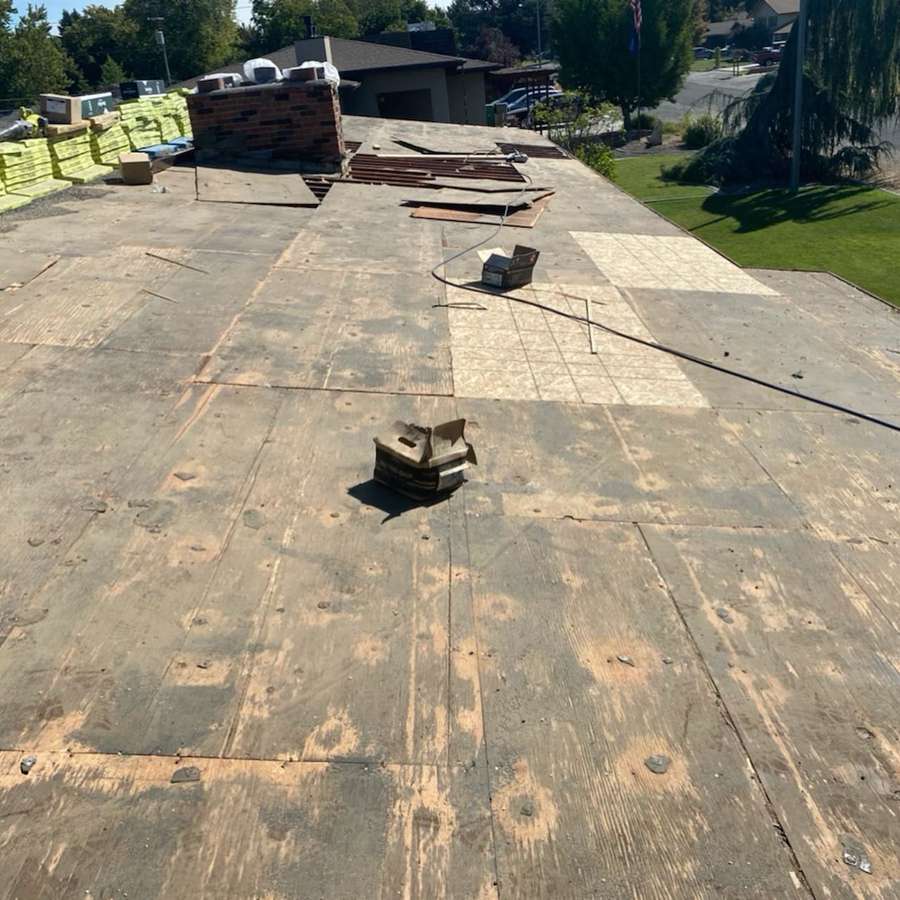 View of a roof with exposed wood and construction debris; some new roofing materials are nearby.