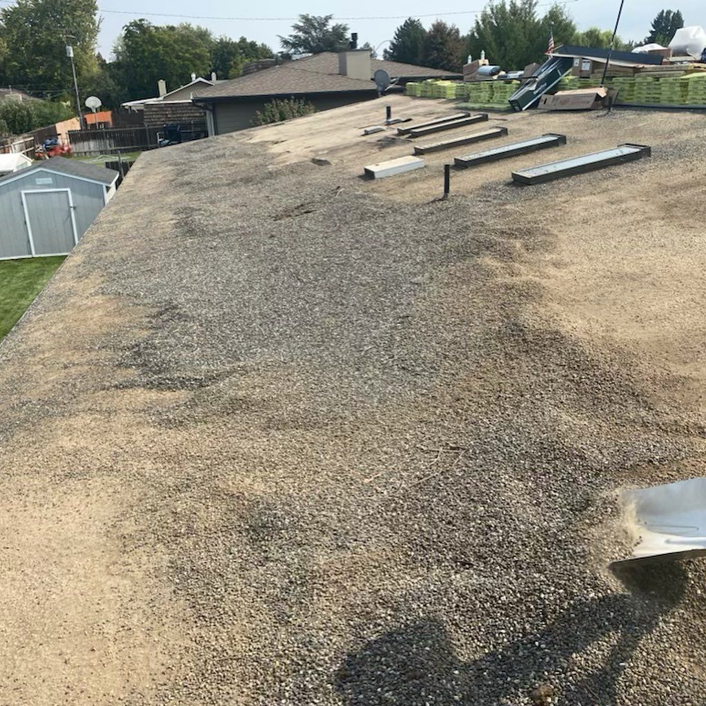 A flat gravel roof with metal vents, set against a residential neighborhood with a shed.