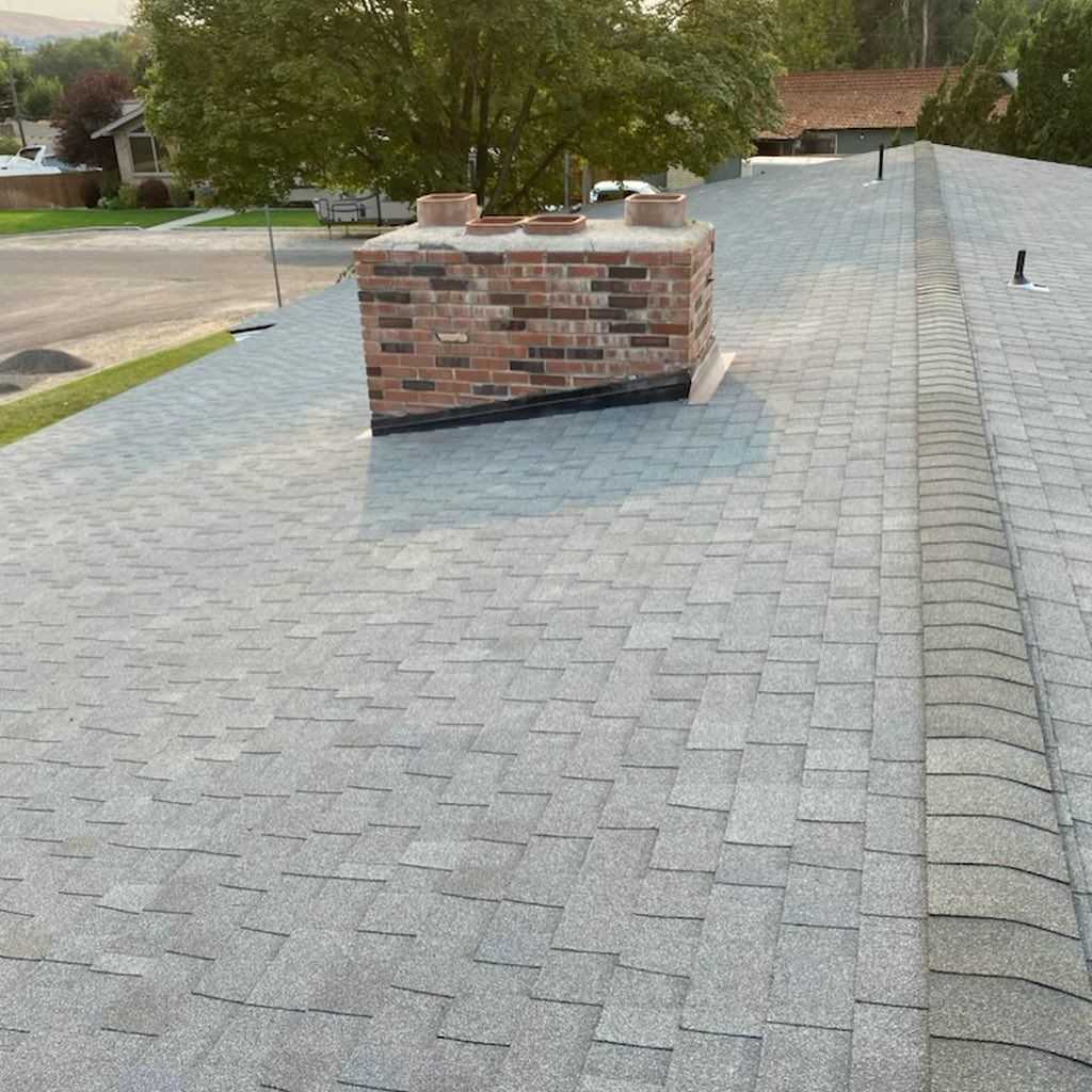Gray asphalt shingle roof with a brick chimney in a residential setting.