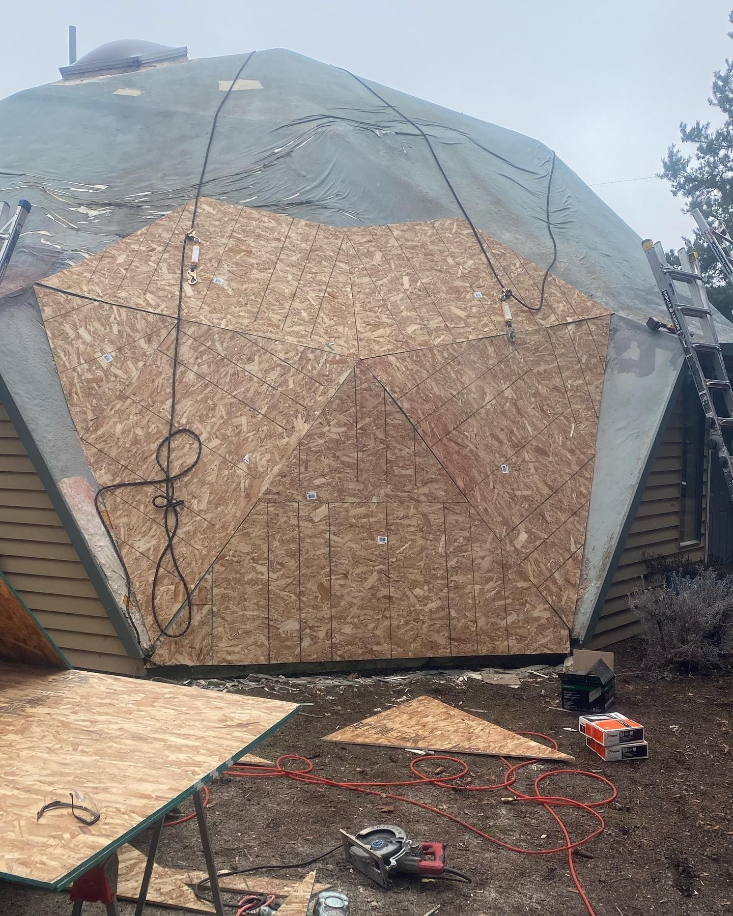 Construction site: Dome-shaped structure with plywood panels being installed. Power tools and materials visible.