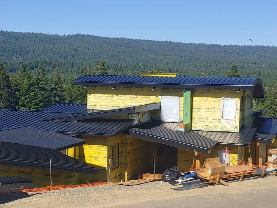 House under construction with black roof and yellow sheathing, mountains in the background.