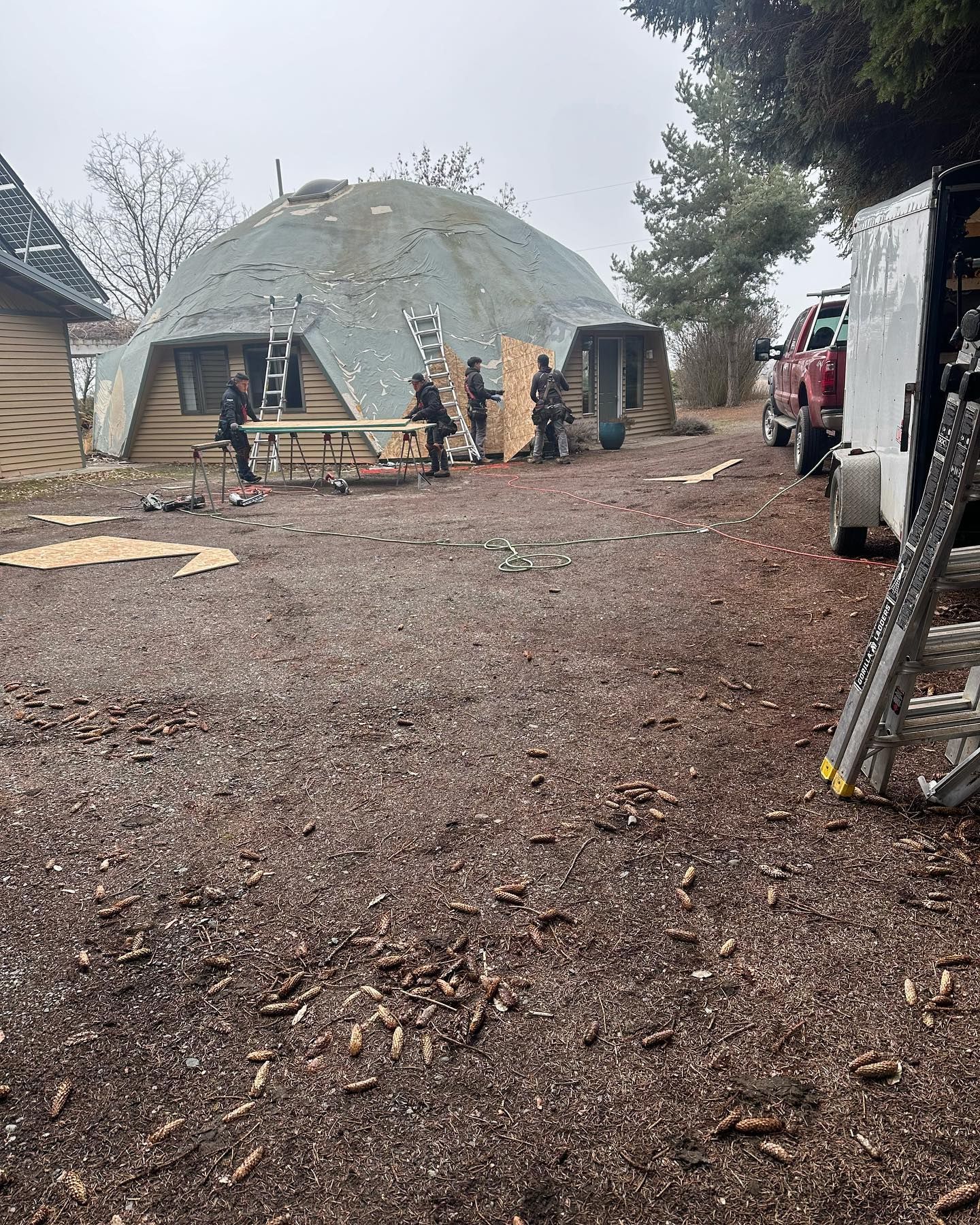 Construction workers near a geodesic dome-shaped building, working with wood on a cloudy day.