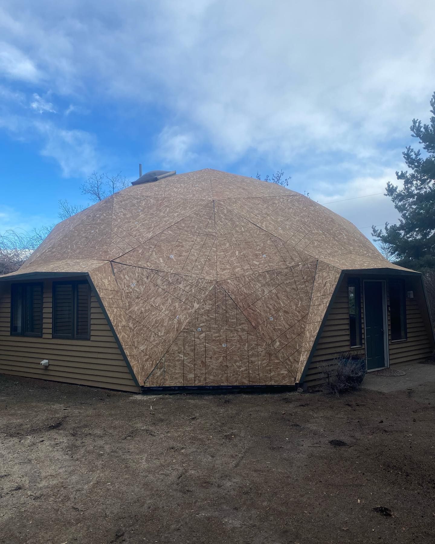 Dome-shaped house with a wooden facade, set against a cloudy sky.