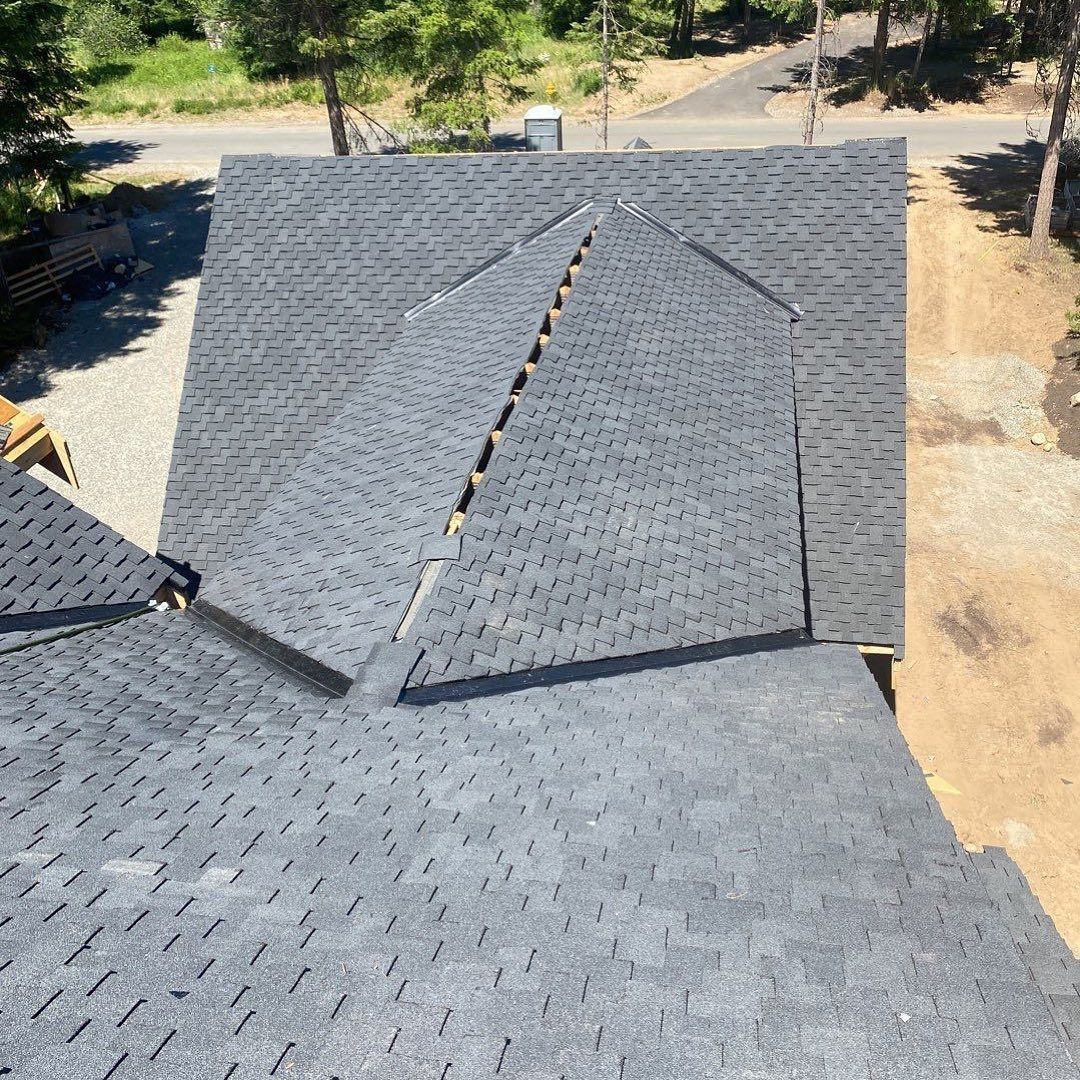 A partially shingled roof with dark grey shingles, seen from above. A section is incomplete.