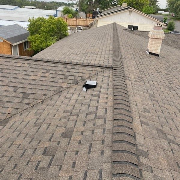Close-up view of a brown asphalt shingle roof with a chimney and vent.