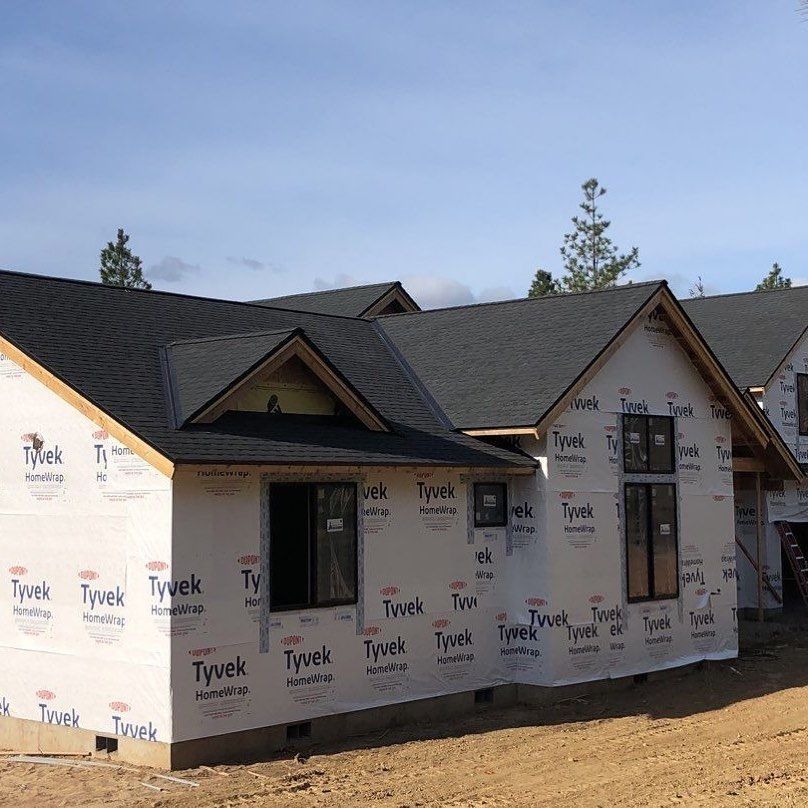 House under construction with black roof and Tyvek wrap against a blue sky.