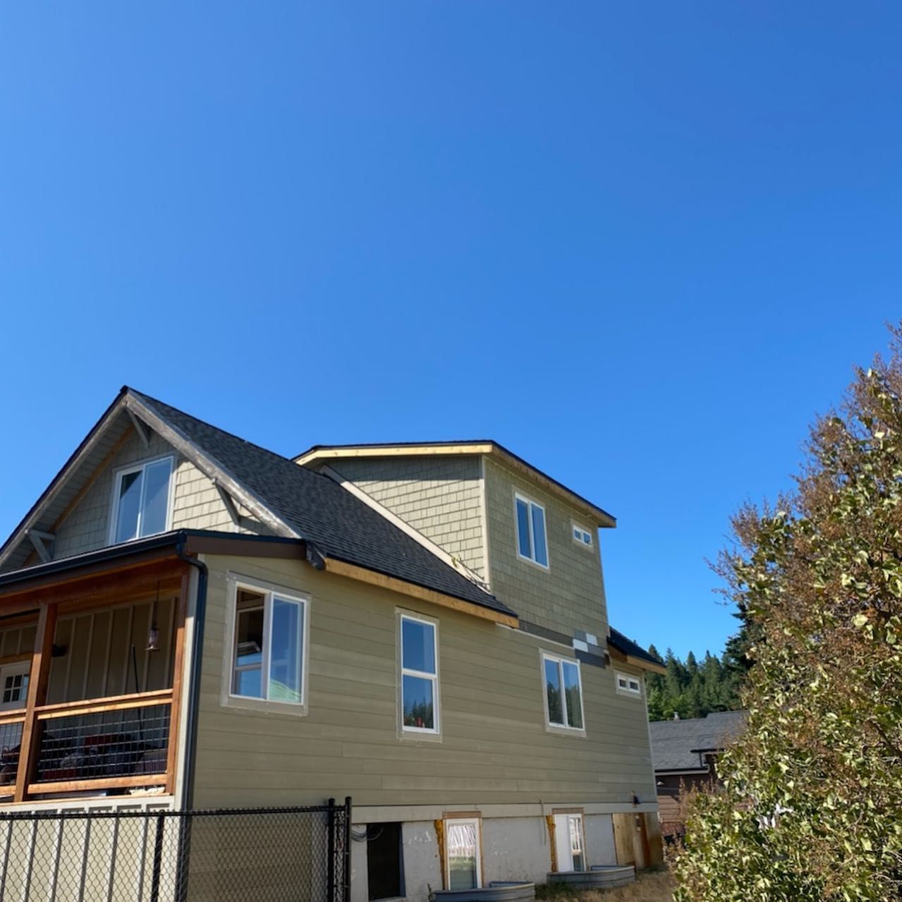 Two-story house under construction with a black roof and light green siding against a clear blue sky.
