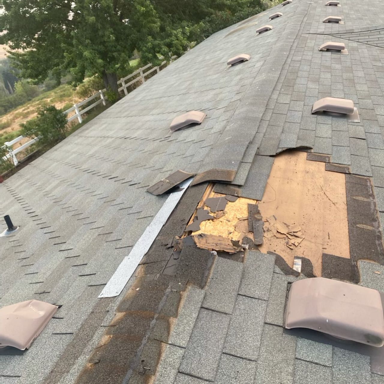 Damaged asphalt shingle roof with missing shingles and exposed wood.