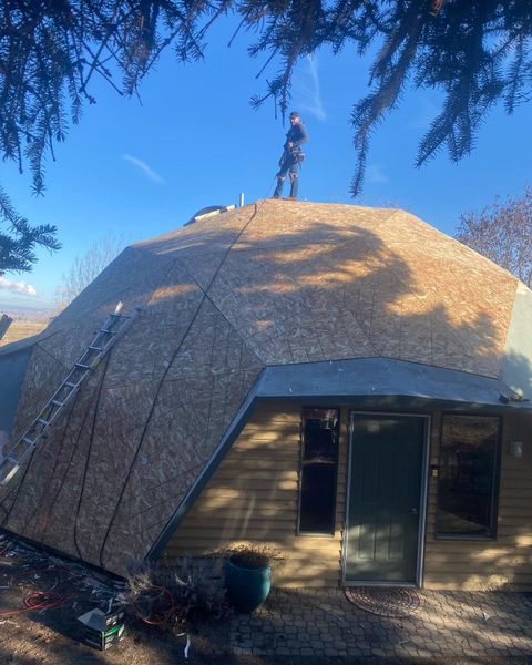 Person on a geodesic dome roof, working on construction. Ladder leans against the side. Blue sky.