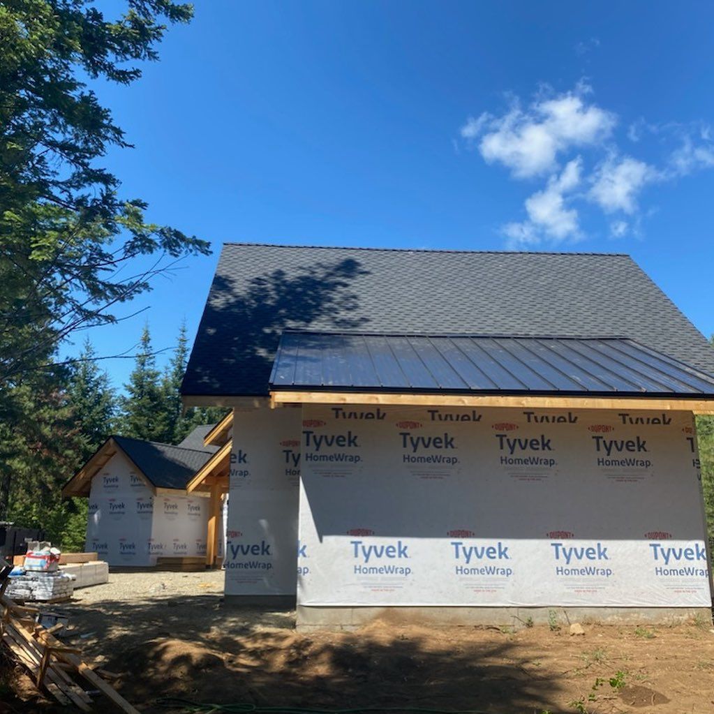 Buildings under construction with black metal roofs and Tyvek wrap against a blue sky.