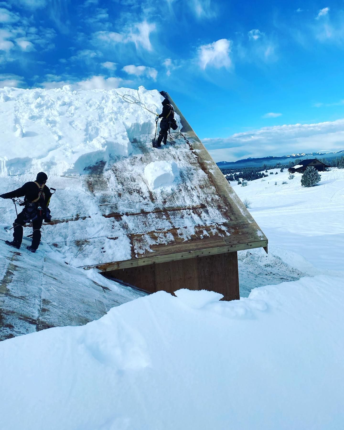 Two people clearing snow from a rooftop on a sunny day.