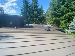 Brown metal roof of a house with trees and a blue sky in the background.