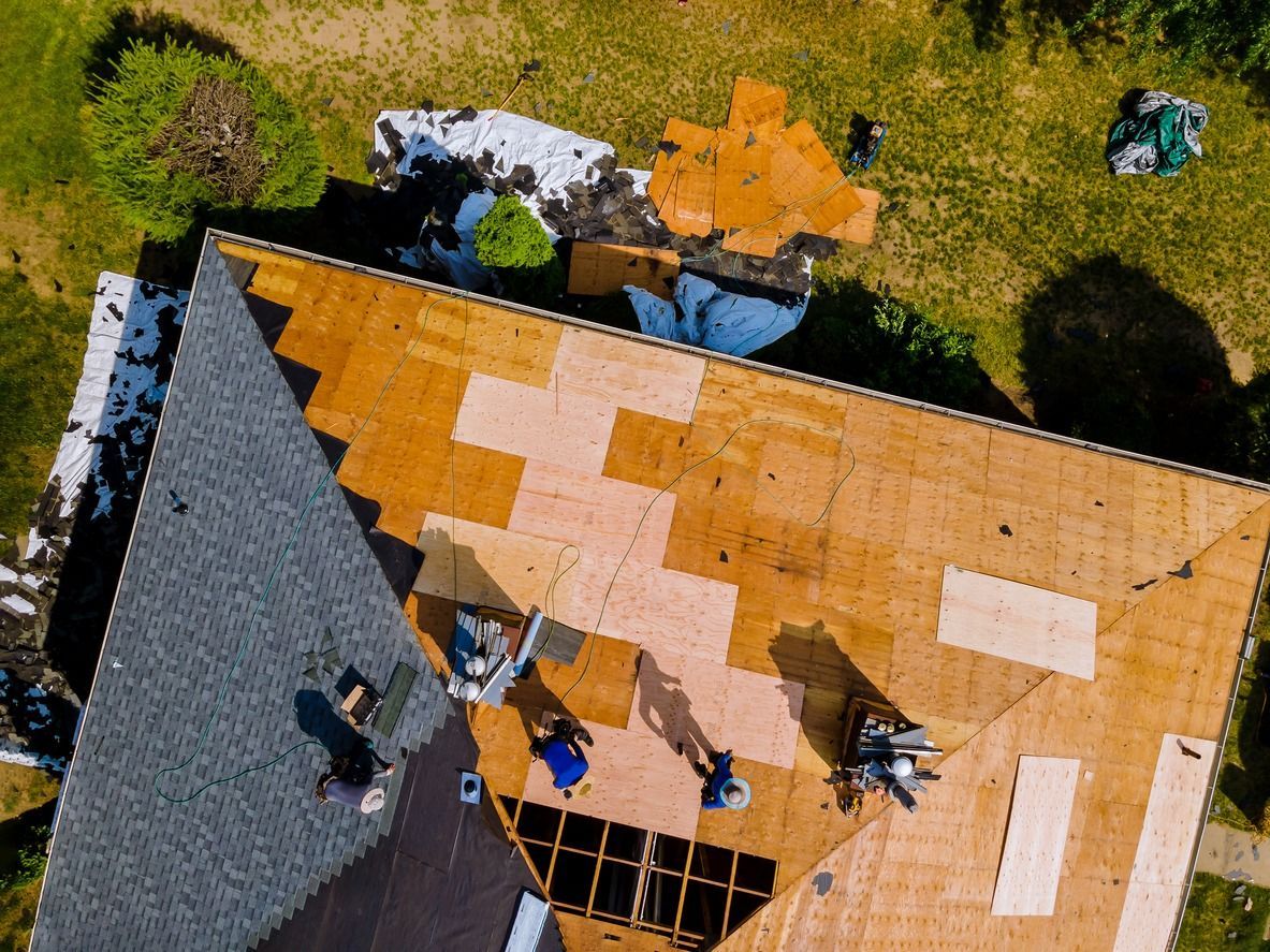 Roofers working on a house roof. Various sections completed, others partially covered with new shingles.