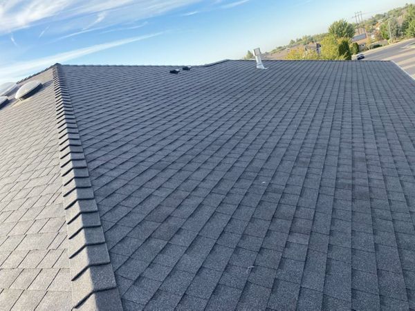 Dark asphalt shingle roof on a house, angled view, with a blue sky background.