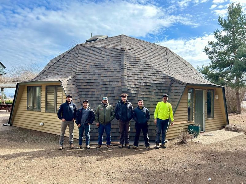 A group of seven people stand in front of a domed building with a blue sky in the background.