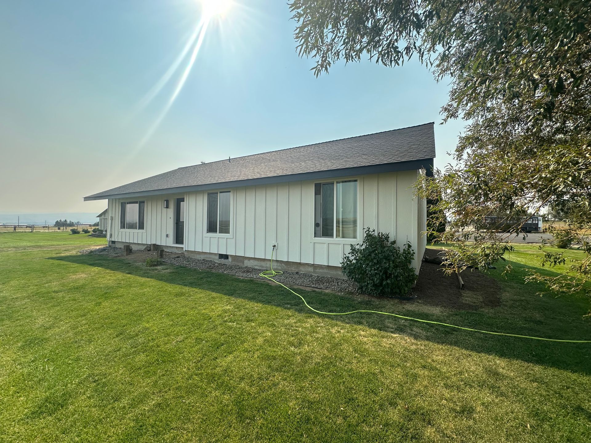 House exterior under construction, tan siding, black roof, blue sky, truck in foreground.