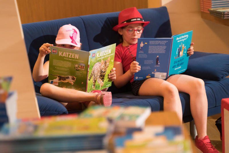 Zwei Kinder sitzen auf einem Sofa und lesen Bücher.