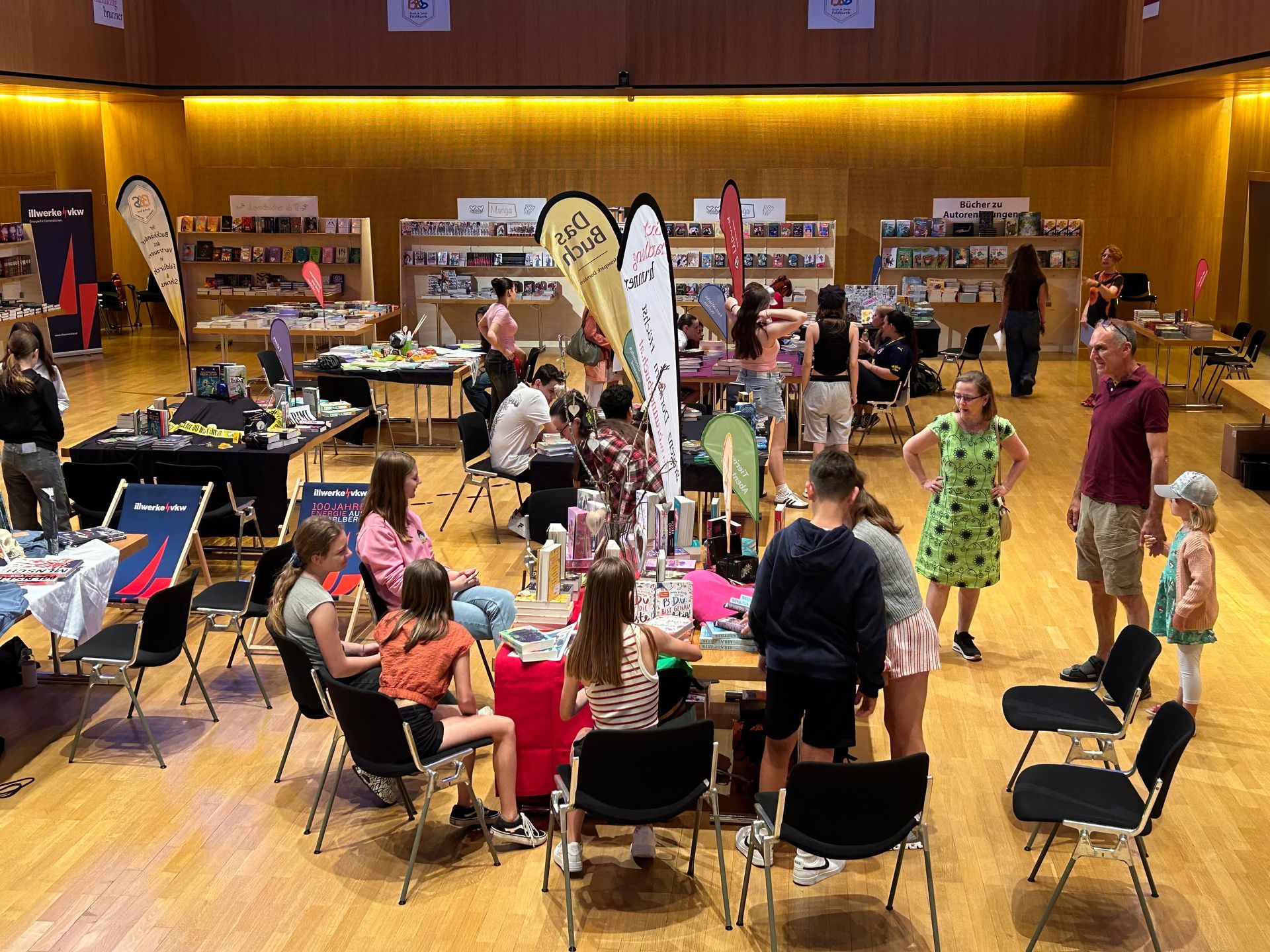 Eine Gruppe von Menschen sitzt in einem großen Raum an Tischen.