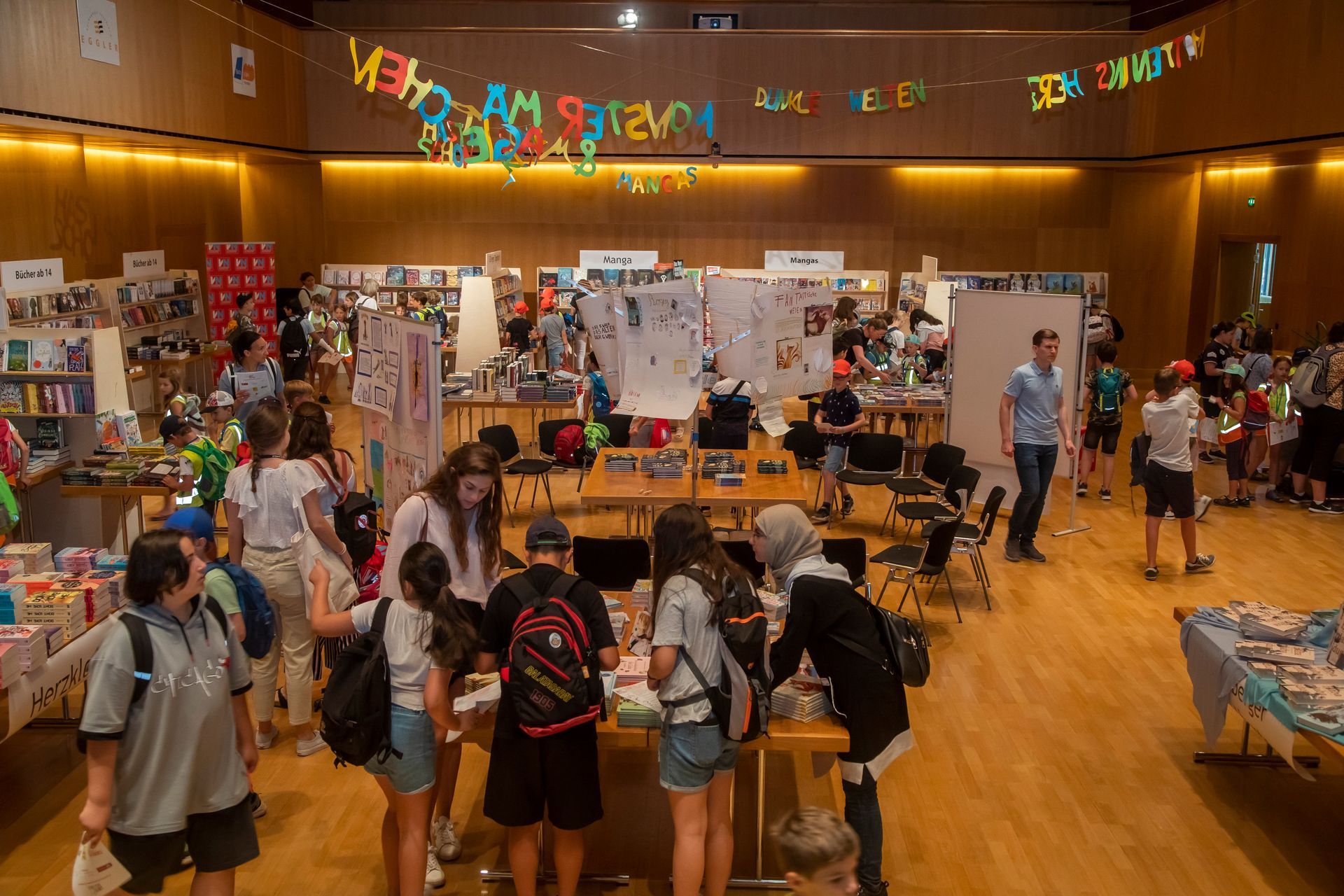 Eine Gruppe von Menschen steht in einem Raum um Tische herum und trägt ein Schild mit der Aufschrift „Ich bin ein System“.