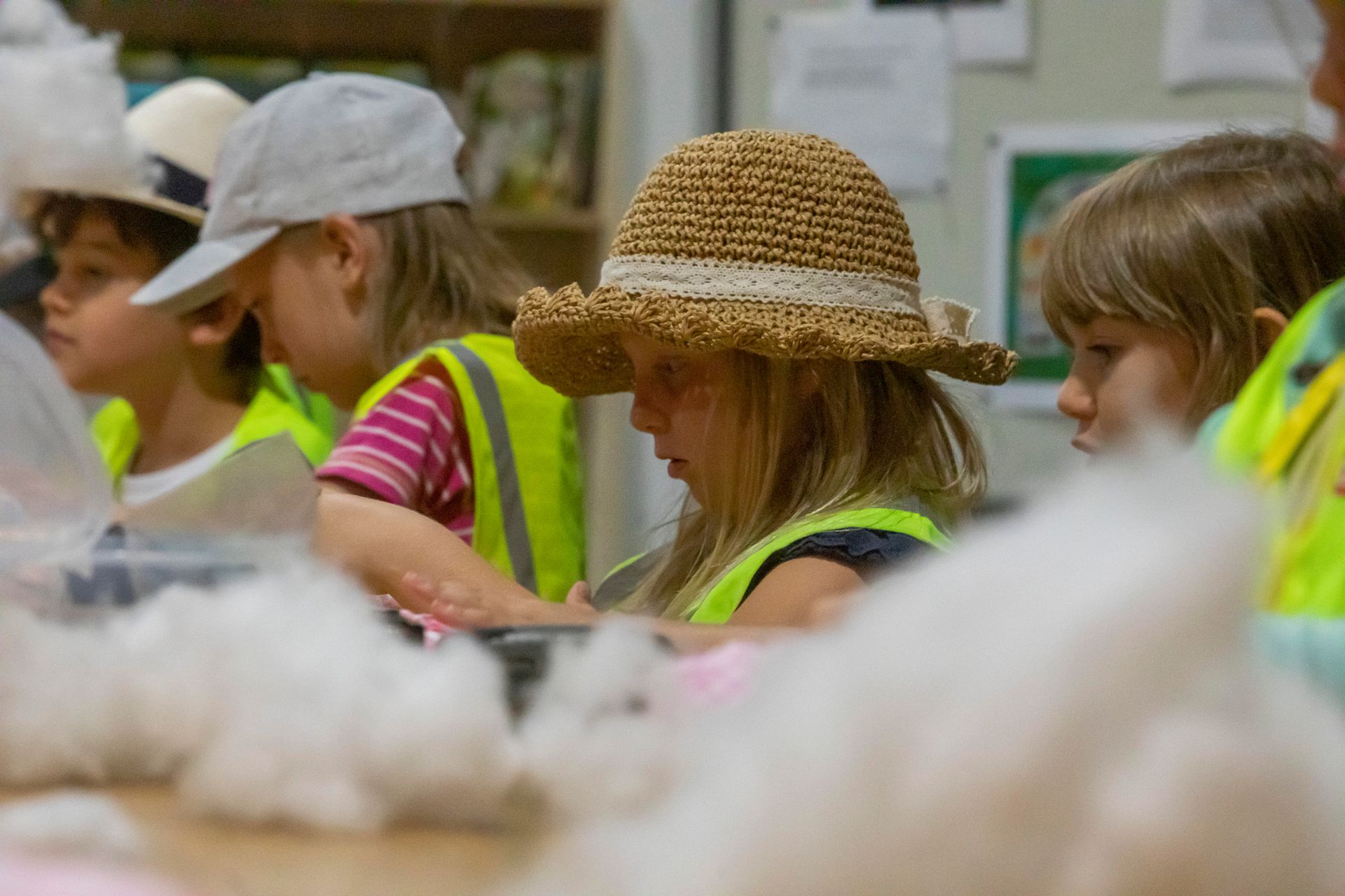 Eine Gruppe von Kindern mit Sicherheitswesten und Mützen sitzt um einen Tisch herum.