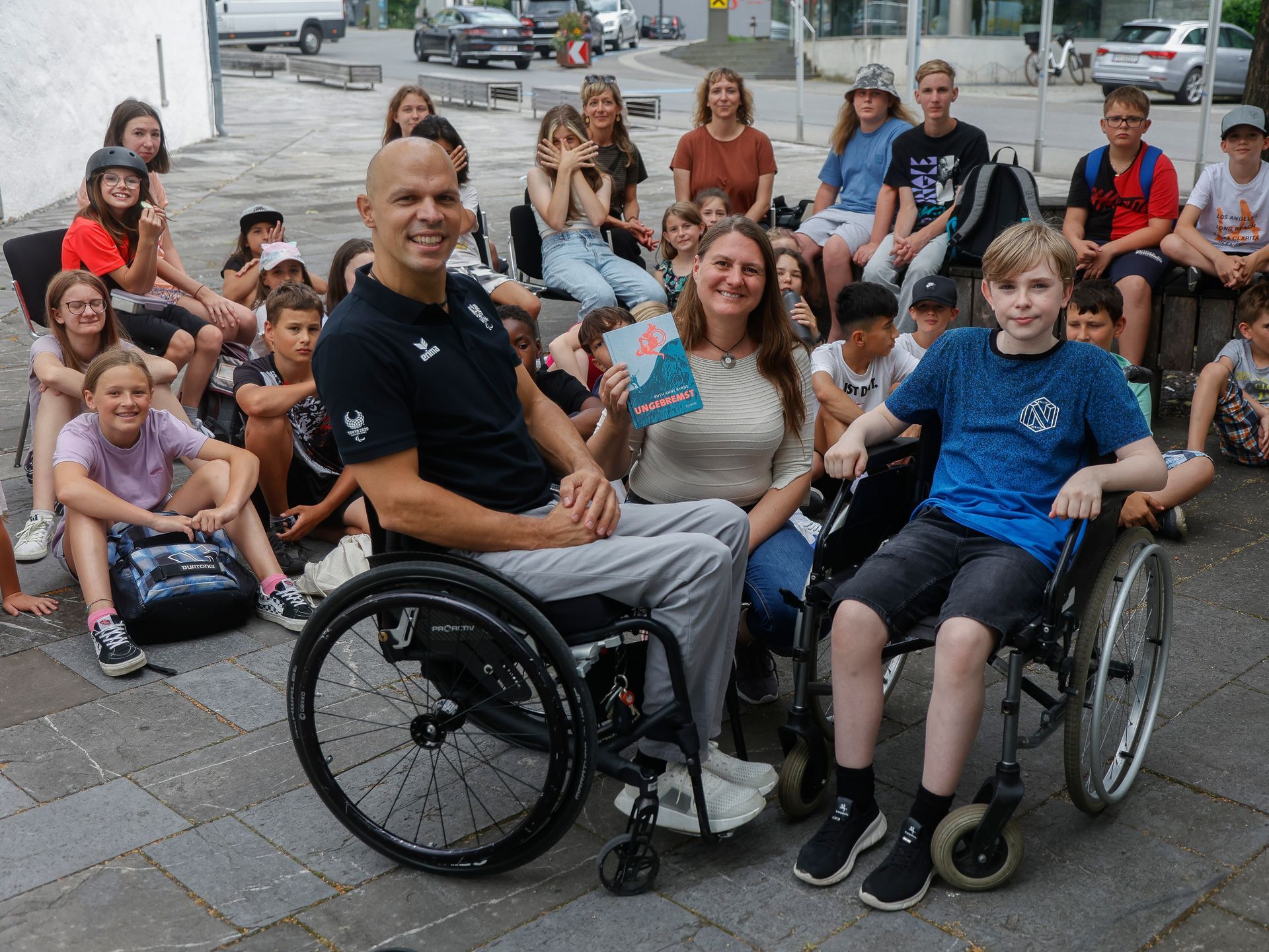 Ein Mann im Rollstuhl sitzt vor einer Gruppe von Kindern