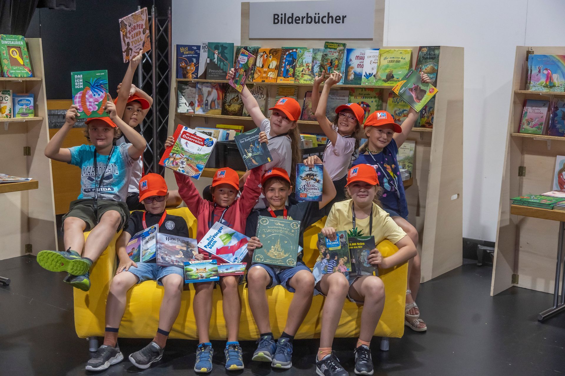 Eine Gruppe Kinder sitzt mit Büchern in den Händen auf einem gelben Sofa.