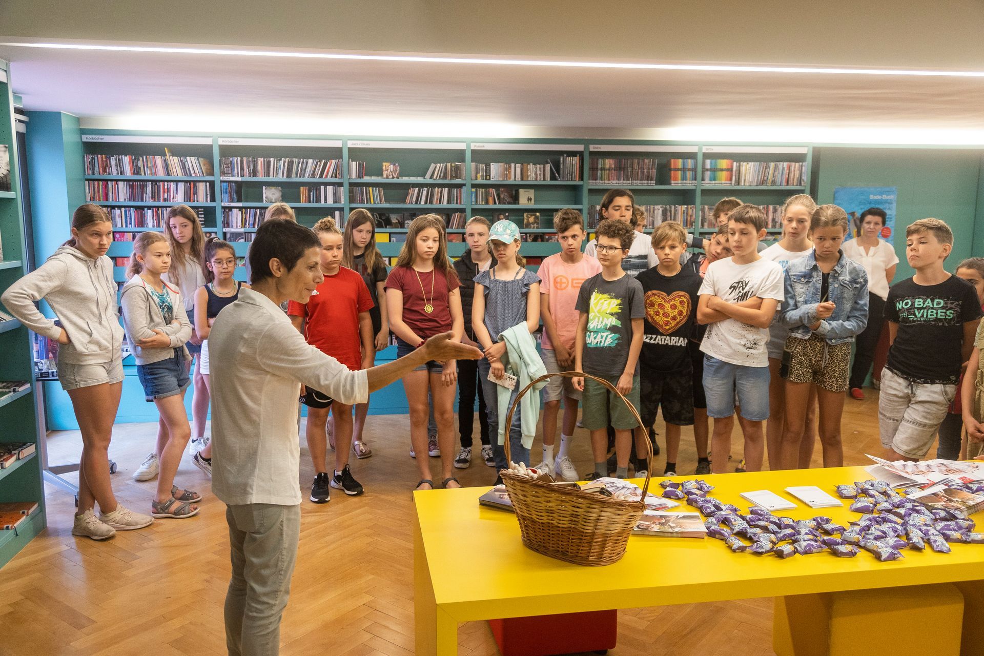 Eine Gruppe Kinder steht in einer Bibliothek um einen Tisch herum.