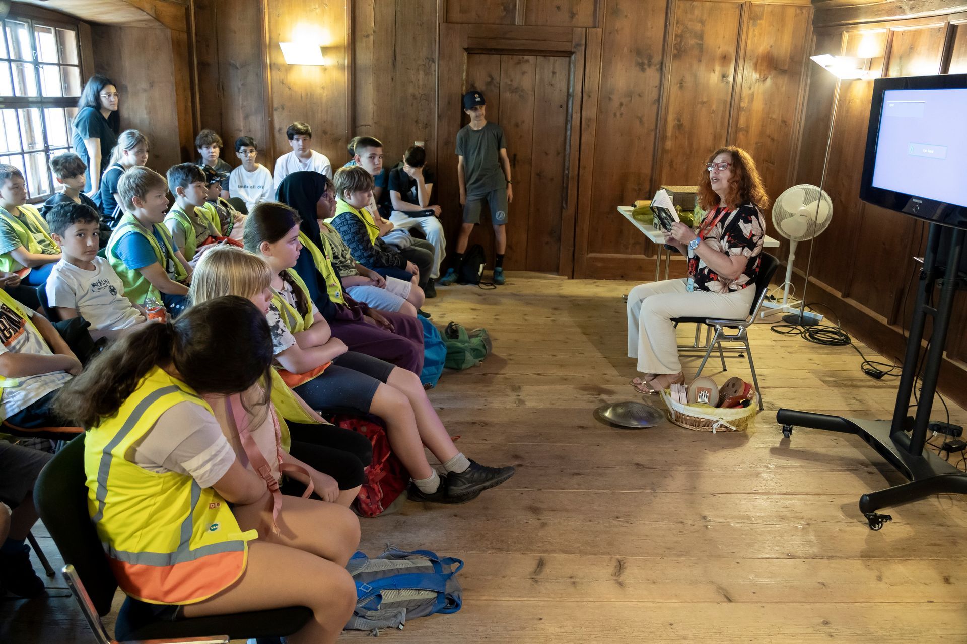 Eine Frau sitzt vor einer Gruppe von Kindern in einem Raum.