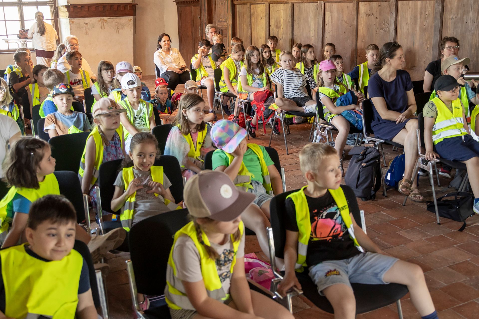 Eine große Gruppe von Kindern sitzt auf Stühlen in einem Raum.