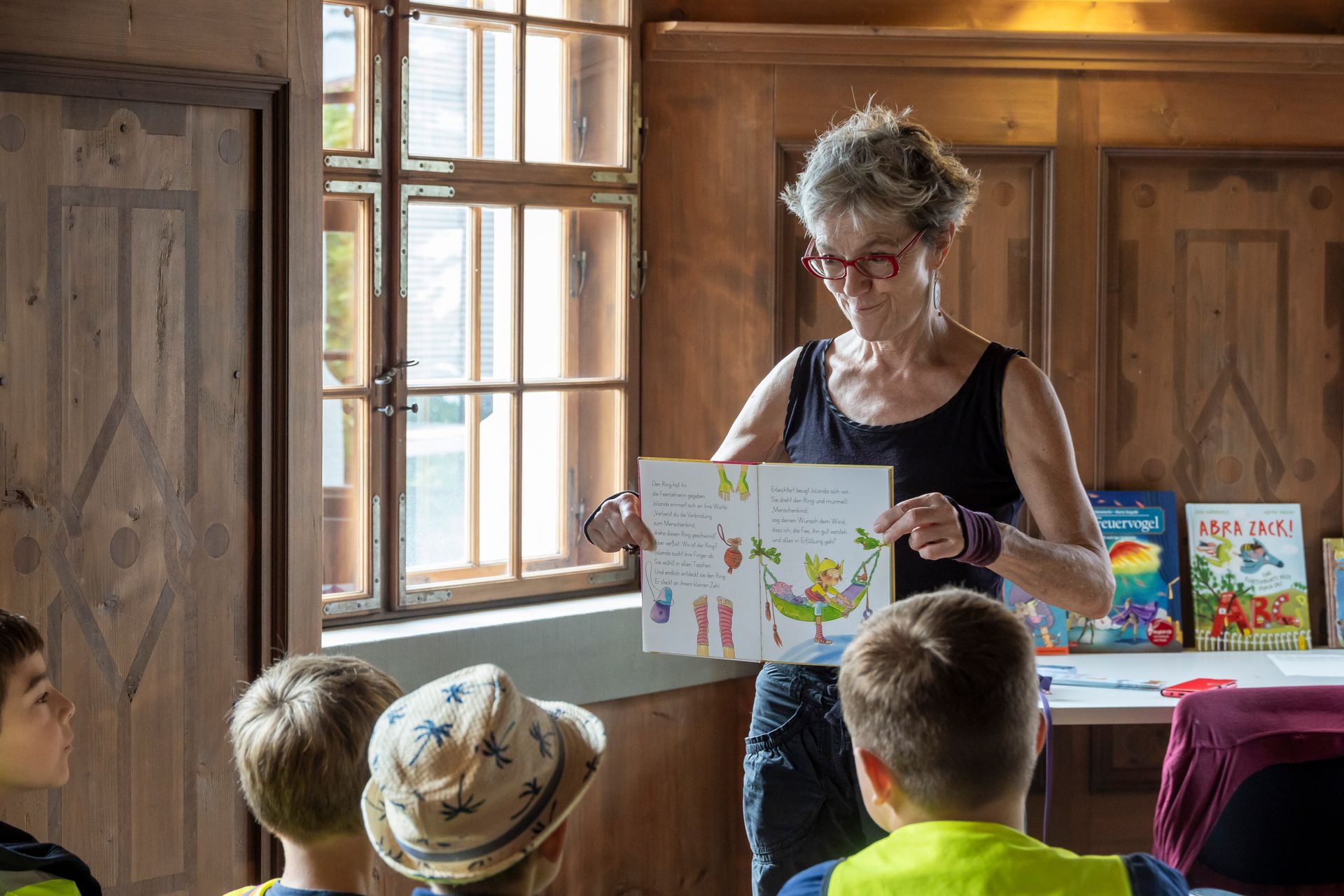 Eine Frau hält vor einer Gruppe von Kindern ein Buch.
