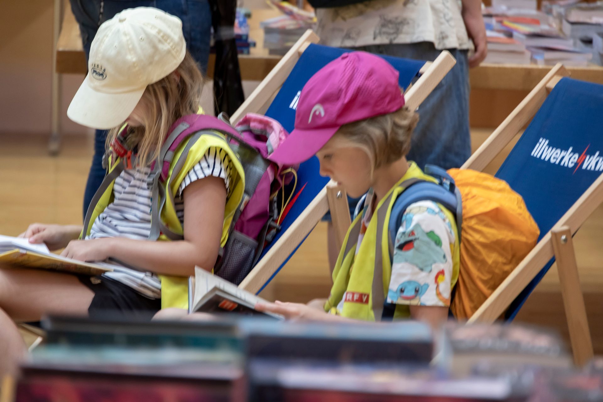 Zwei Kinder sitzen in Gartenstühlen und lesen Bücher.