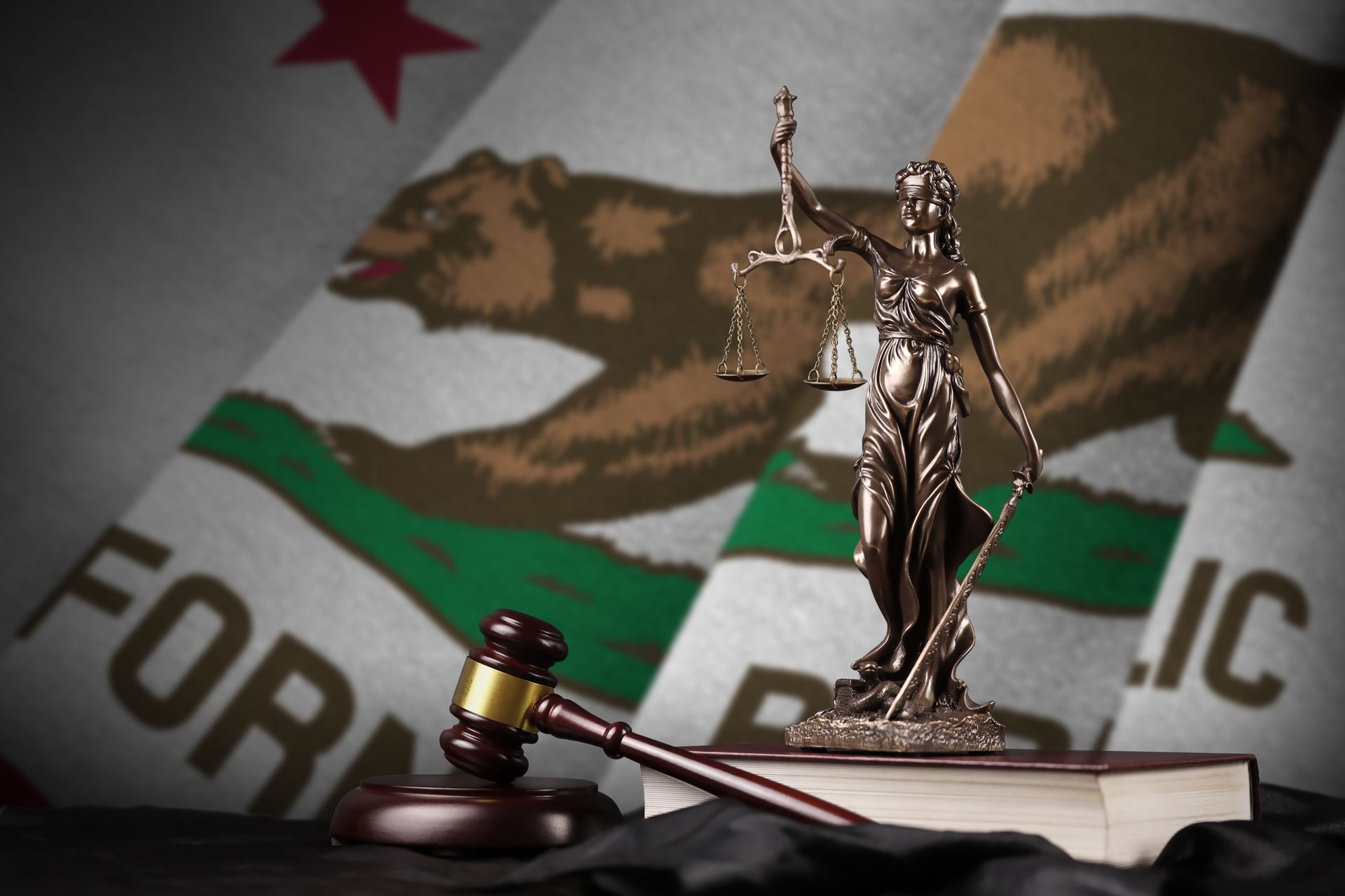 Statue of Lady Justice with scales, gavel, and books, in front of the California flag.