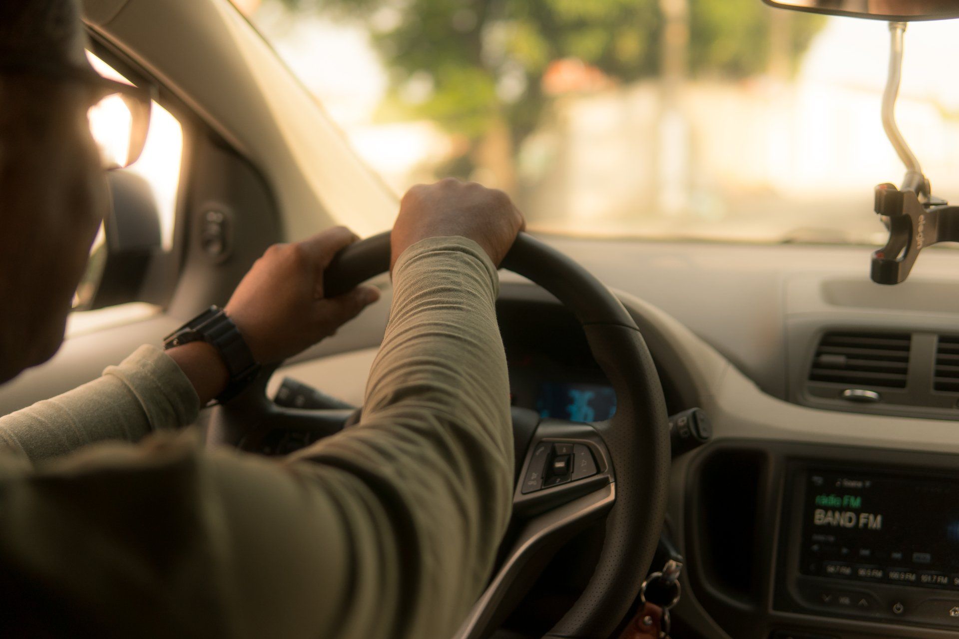 Person's hands gripping a steering wheel while driving. Radio on, daylight through windshield.