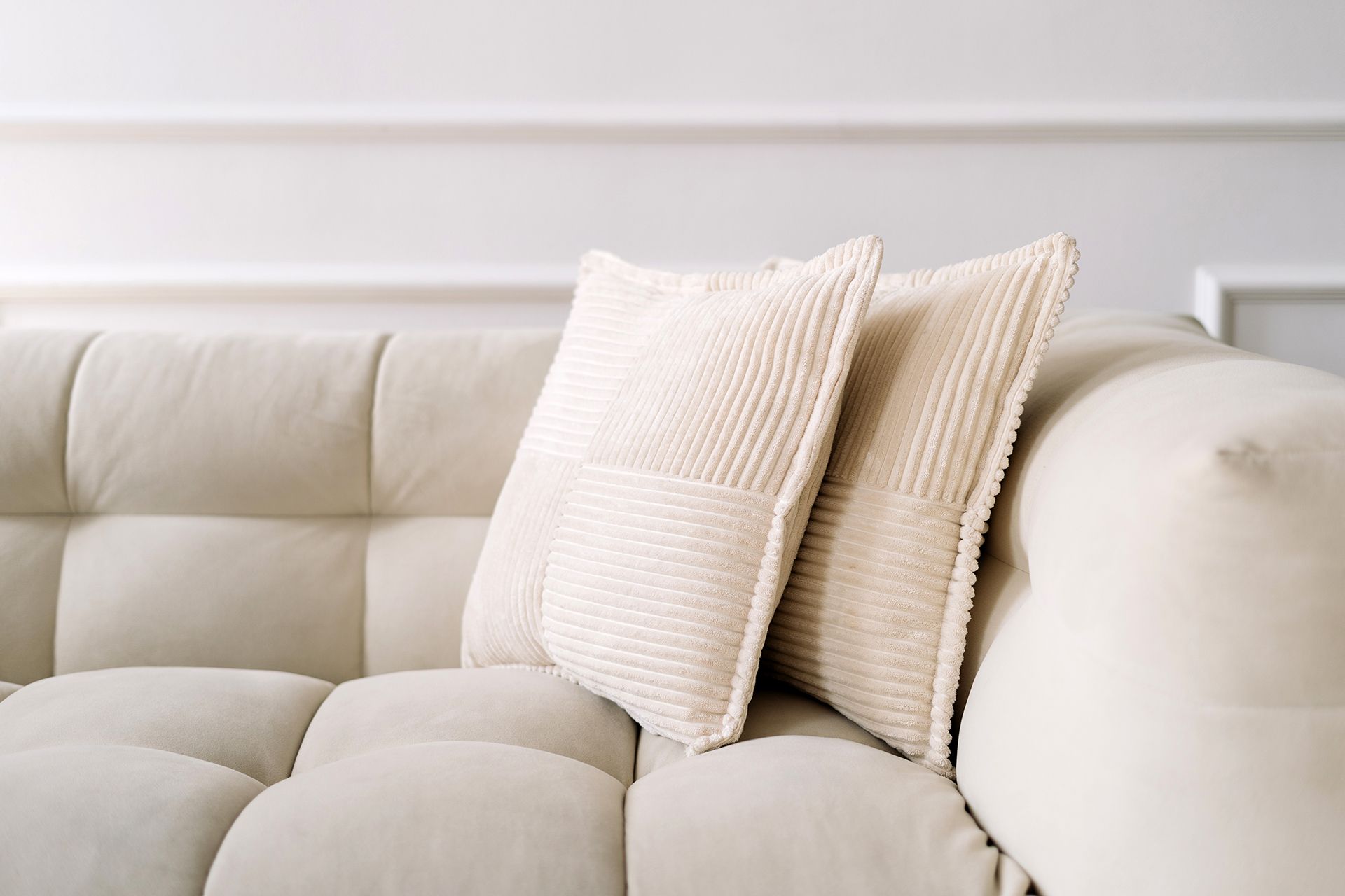 A white couch with three white pillows on it in a living room.