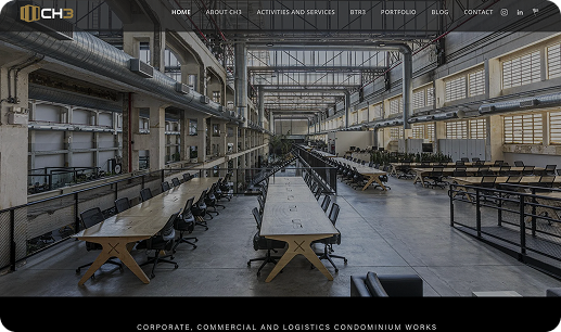 Grande espaço de escritório industrial com mesas e cadeiras longas.