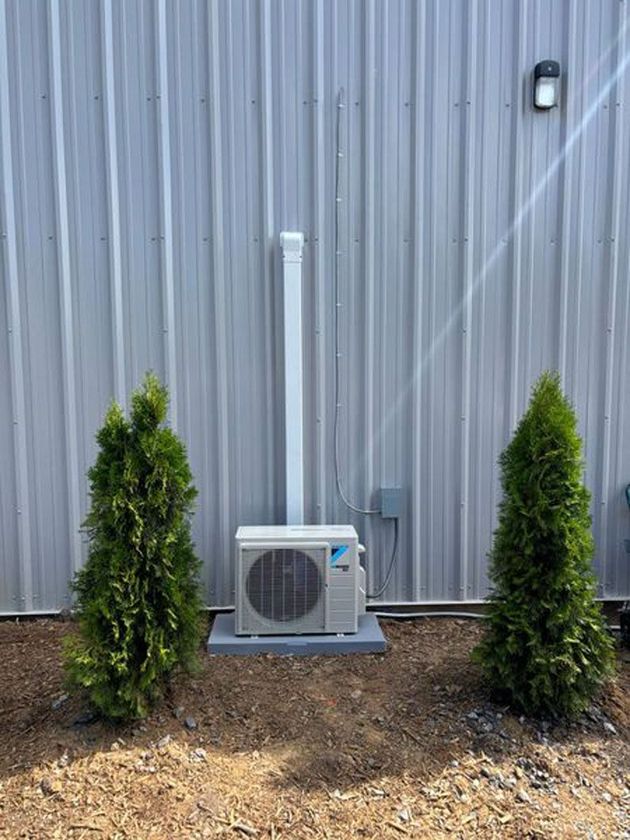 A small air conditioner is mounted on the side of a building next to some trees.