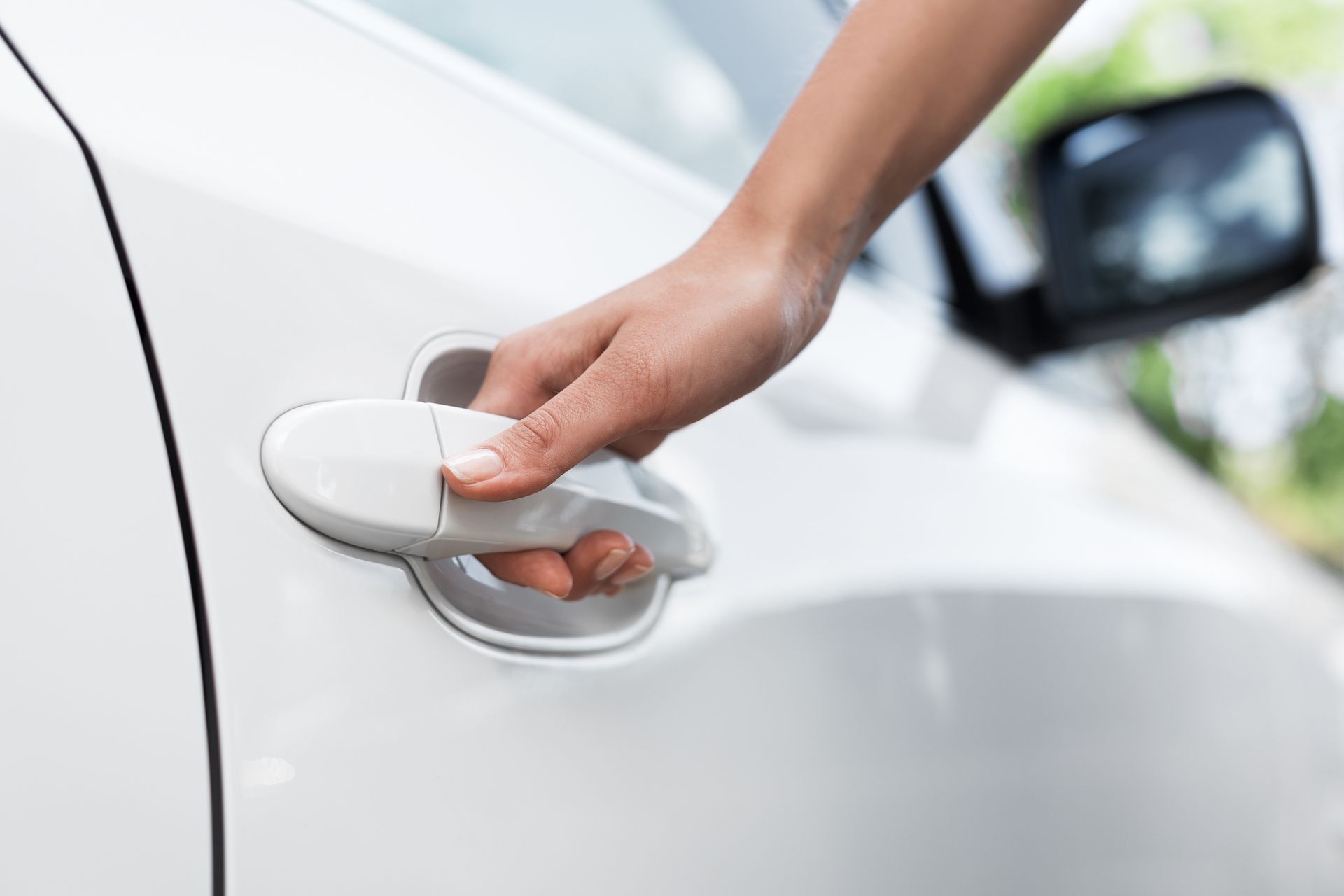 A hand pulls the door handle of a white car to open it.
