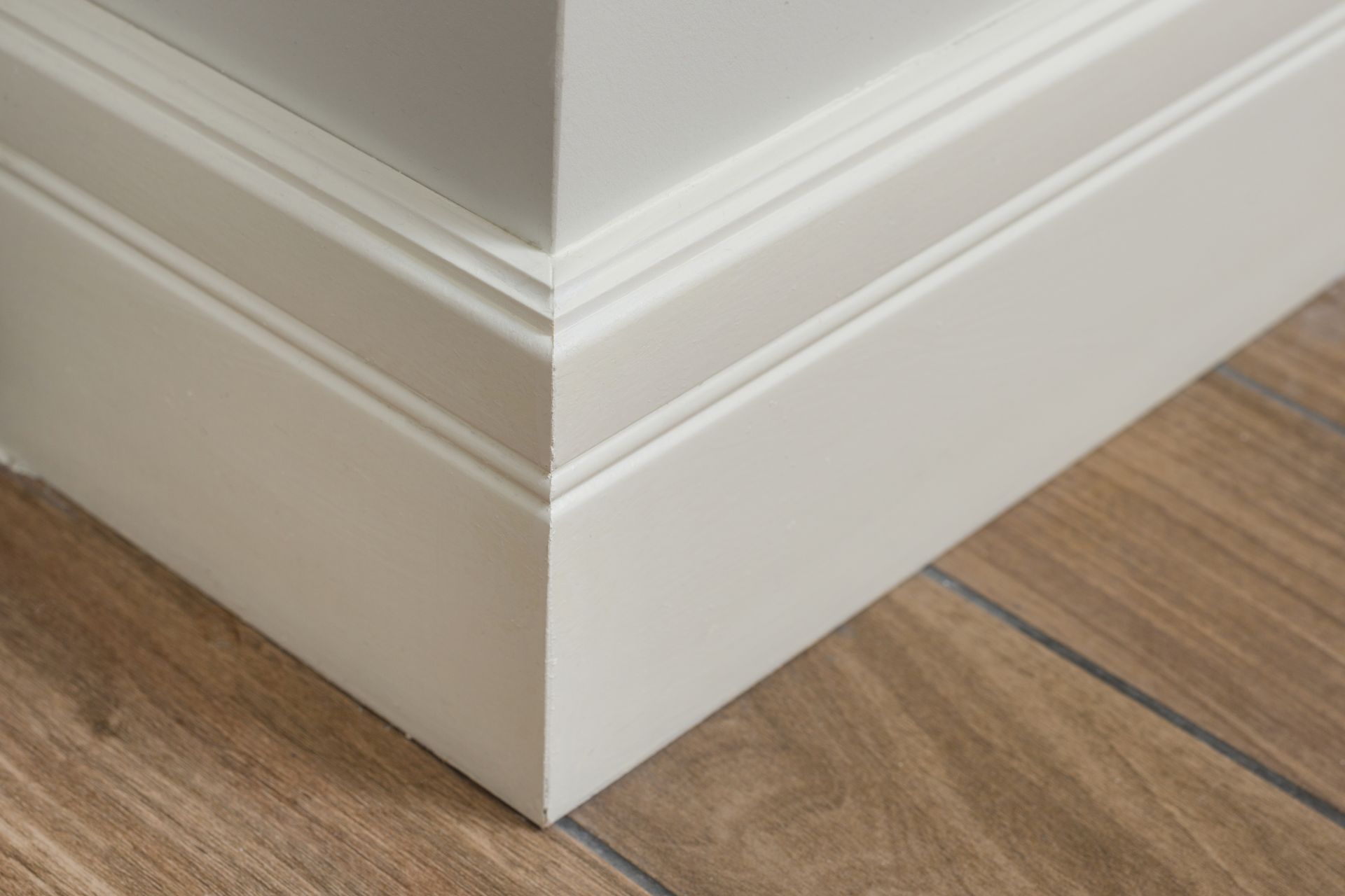 White painted molding and baseboards meet at a corner, above wood flooring.