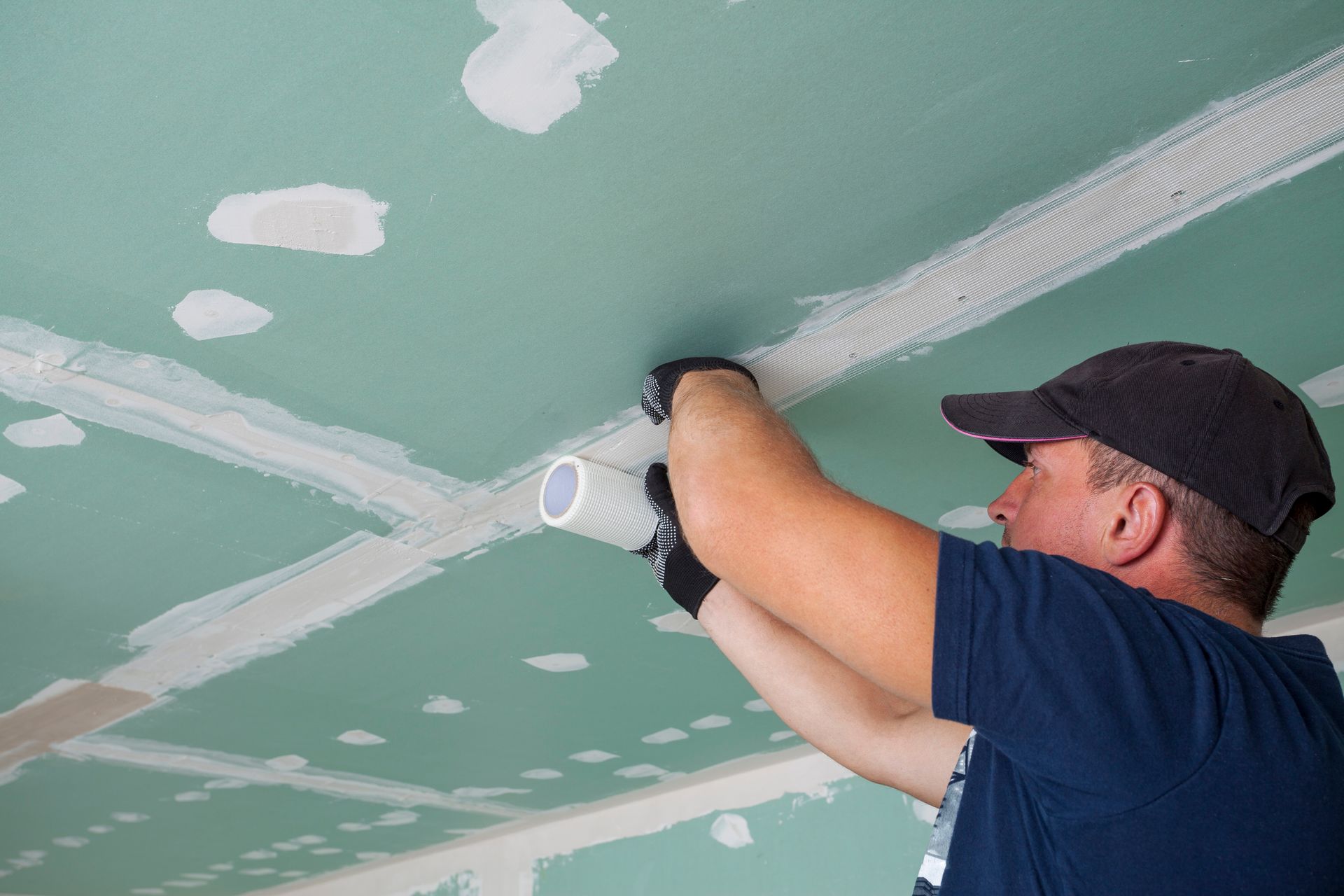 Person installing electrical conduit on a green drywall ceiling.