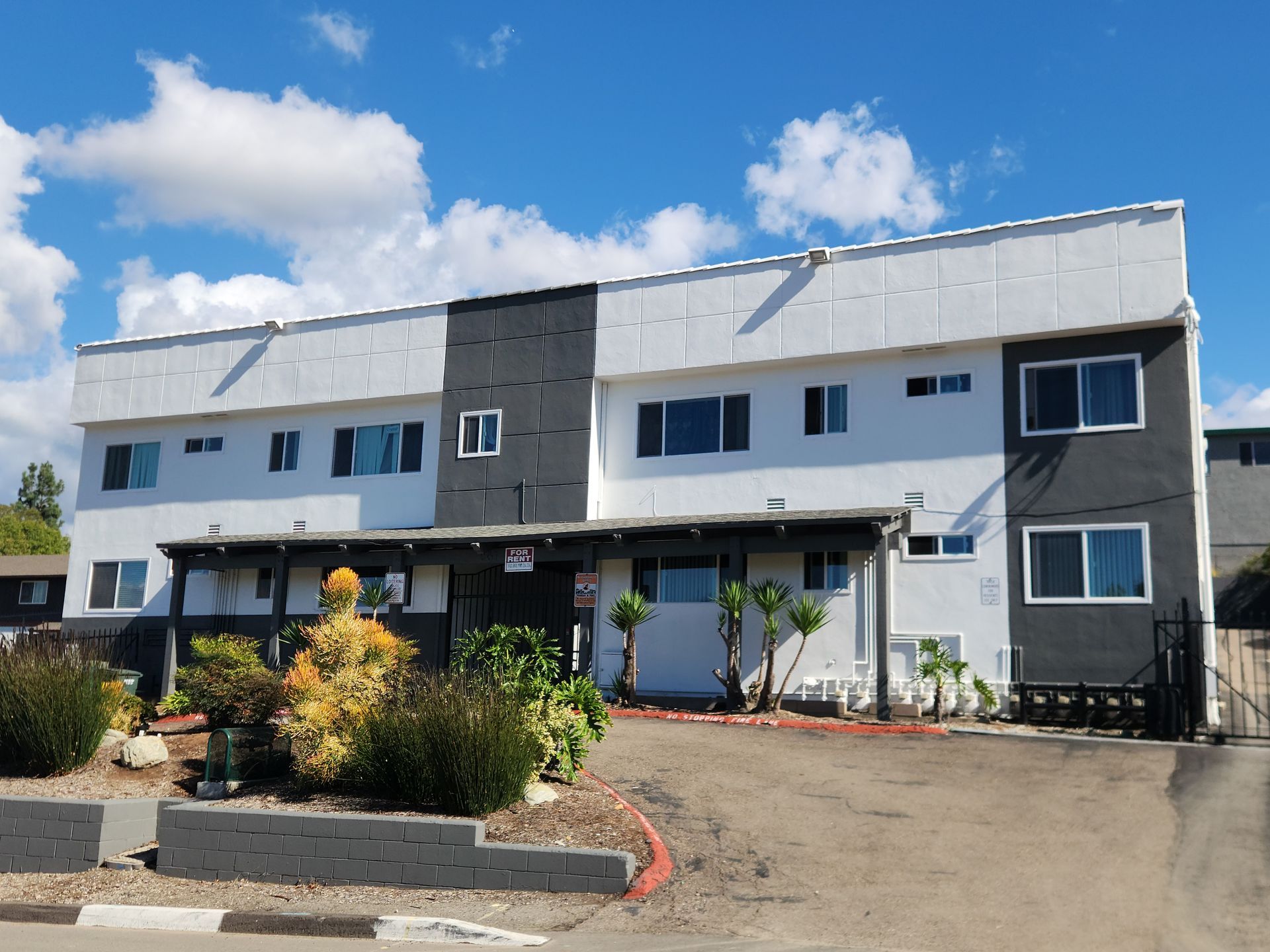 Apartment building with white and gray exterior, under a blue sky with clouds.