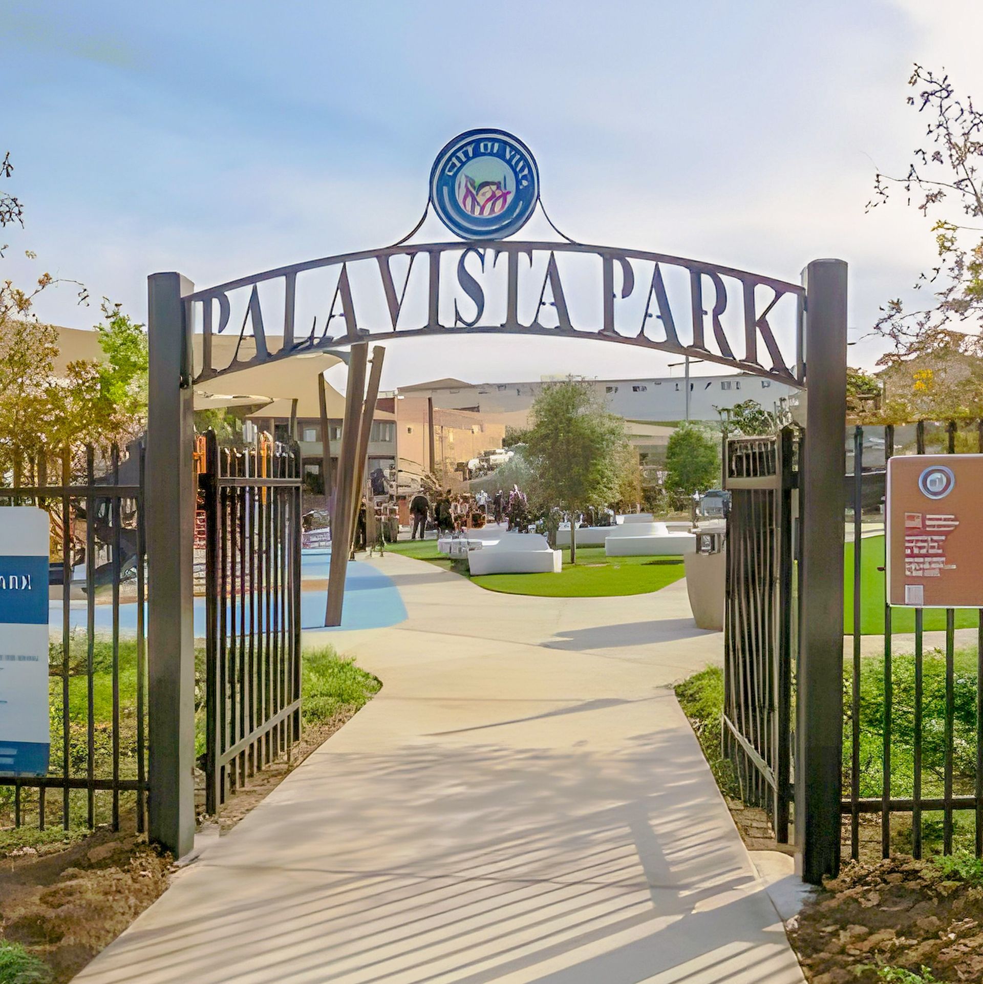 Entrance to Palavista Park with a metal archway, blue sky, and people in the background.