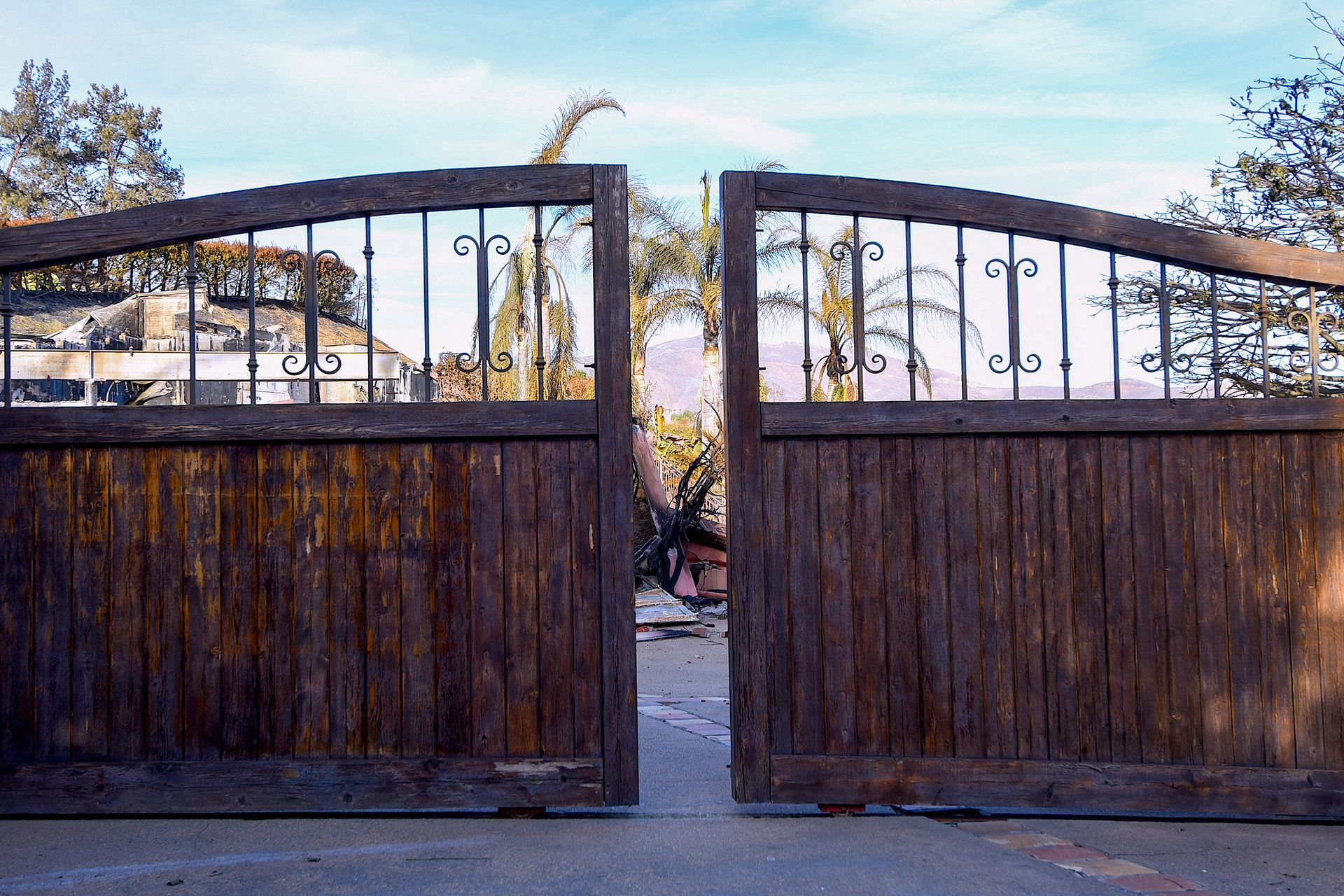 A wooden gate with a wrought iron frame is open to a driveway.