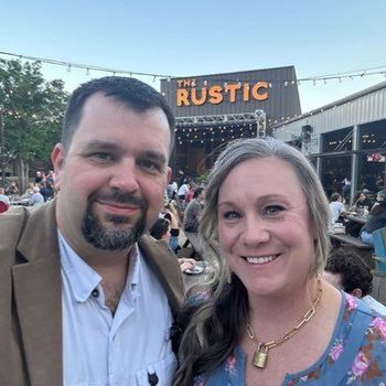 A man and a woman are posing for a picture in front of a building that says the rustic.