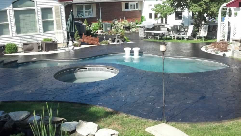 Backyard pool with dark stone deck, round spa, and homes in the background